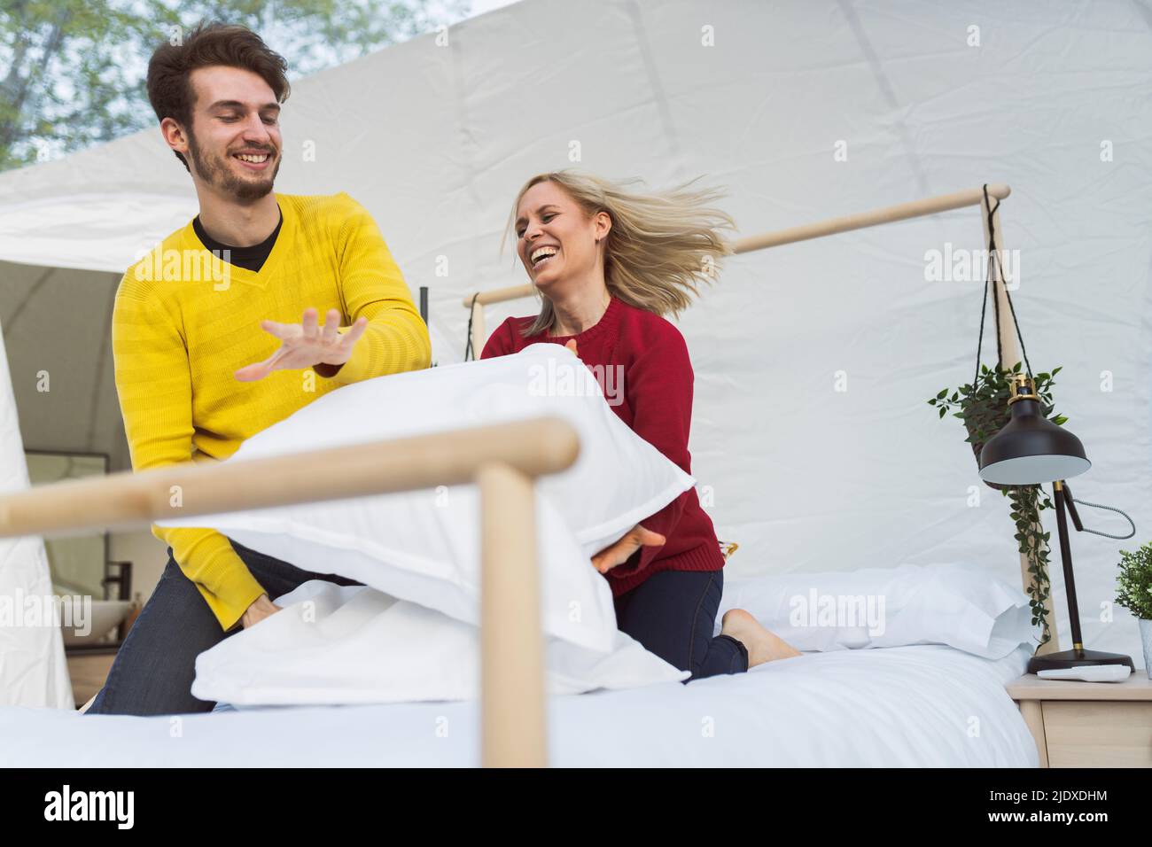 Cheerful couple enjoying pillow fight on bed in hotel room Stock Photo