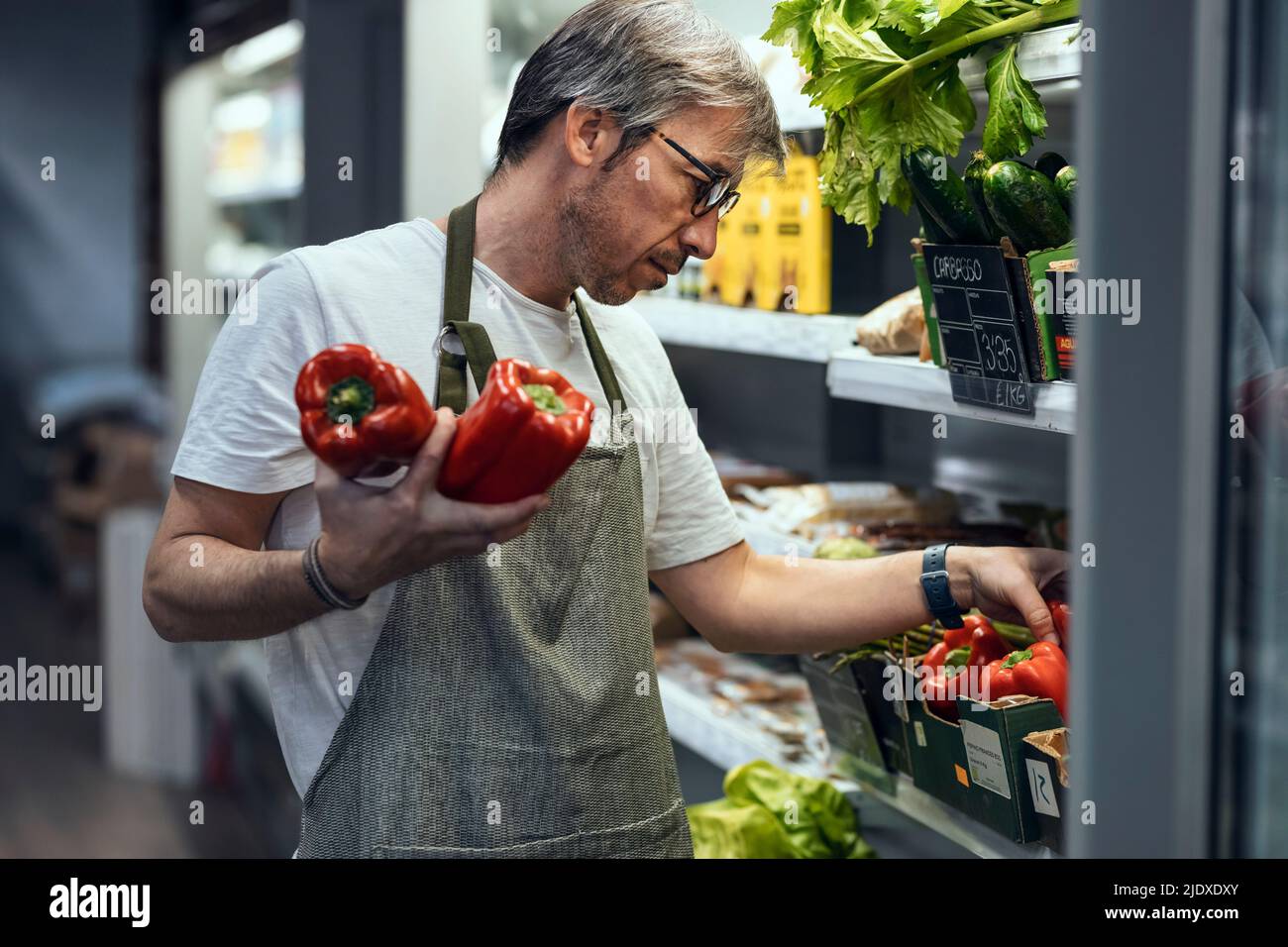 Store owner arranging red bell pepper in rack at organic market Stock Photo