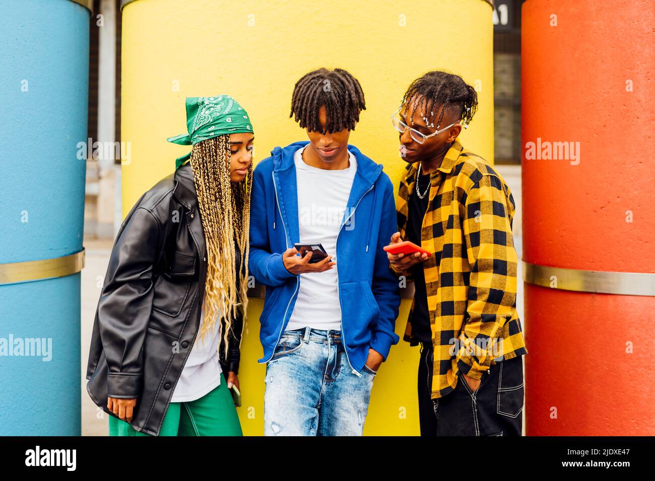 Young man sharing smart phone with friends in front of yellow pipe Stock Photo