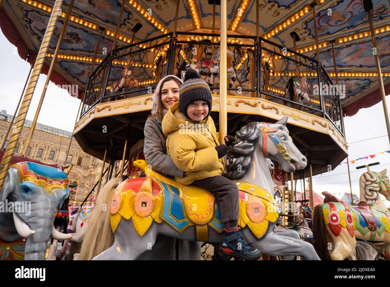 Smiling boy on carousel horse by mother in Christmas market Stock Photo