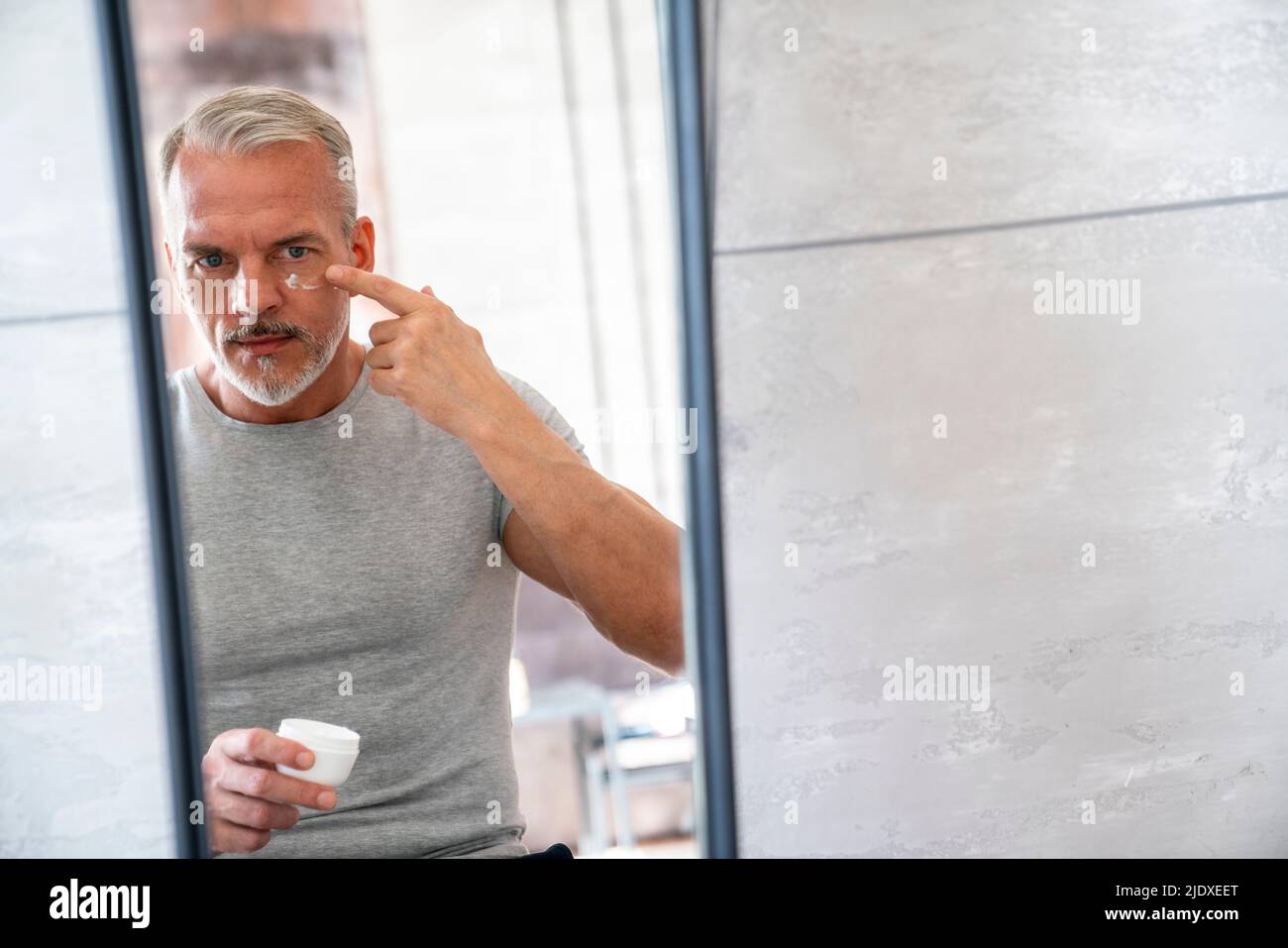 Man applying on moisturizer face looking at mirror in bathroom Stock Photo