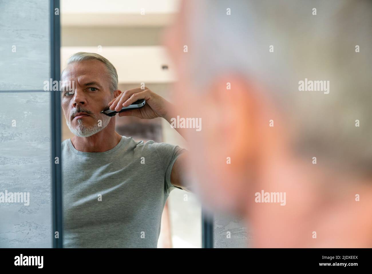 Man shaving beard with electric razor looking at mirror Stock Photo