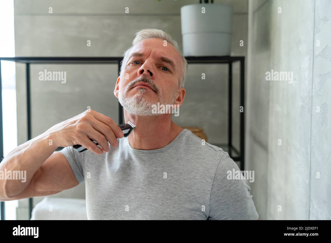 Man shaving beard with electric razor in bathroom Stock Photo Alamy