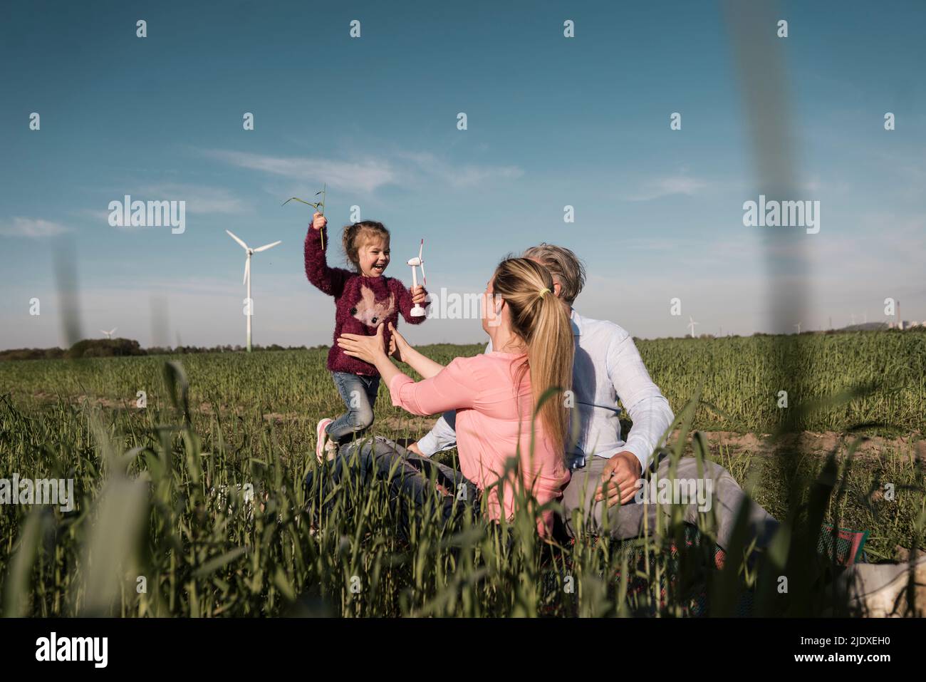 Playful girl holding wind turbine model running towards parents in field Stock Photo