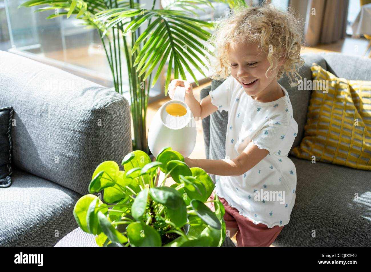 Smiling girl with blond hair watering plant at home Stock Photo - Alamy