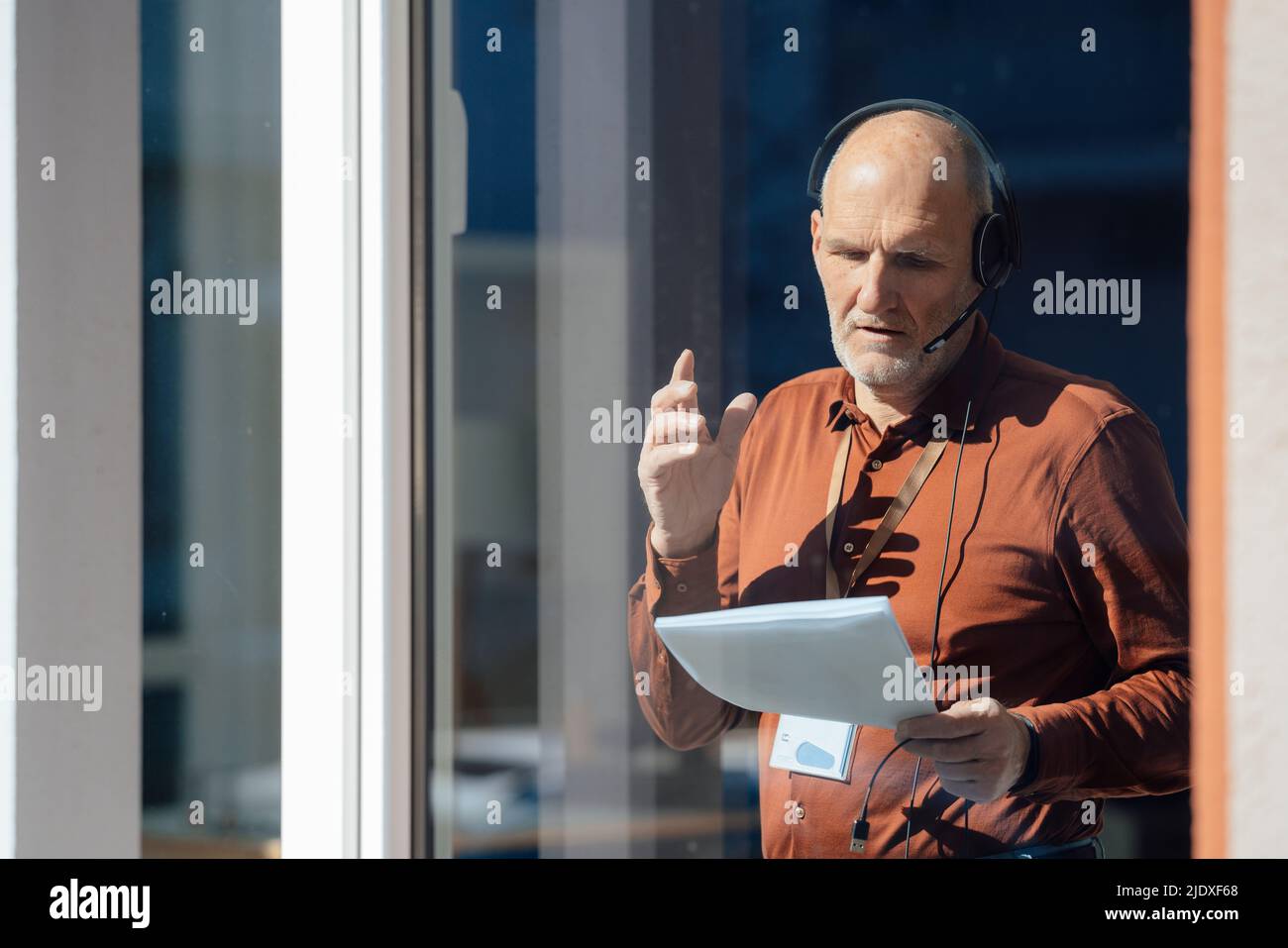 Businessman wearing headset analyzing document seen through glass Stock Photo