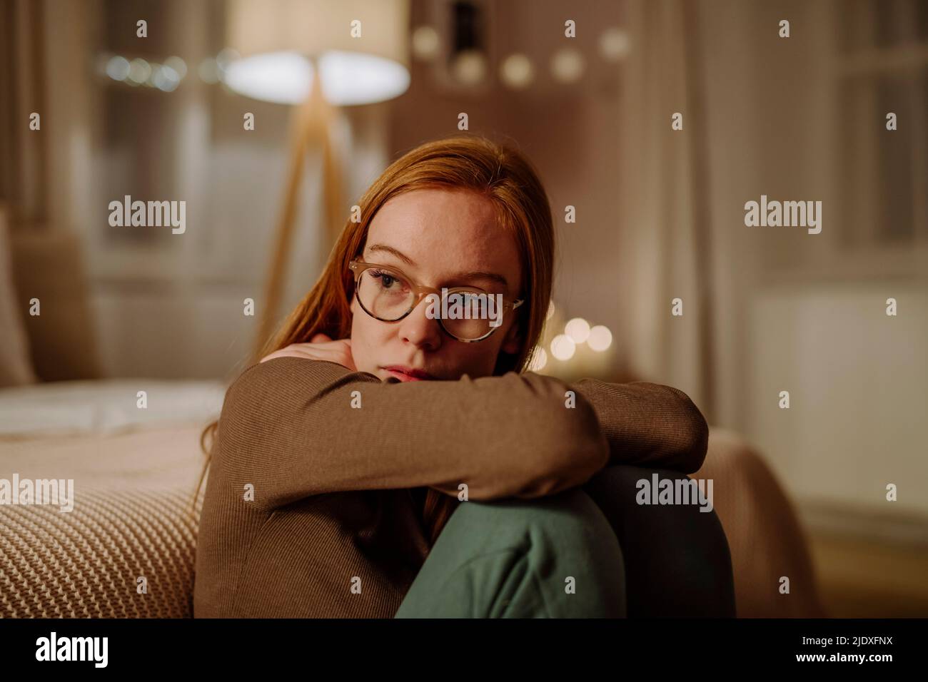 Sad redhead woman sitting in front of bed at home Stock Photo
