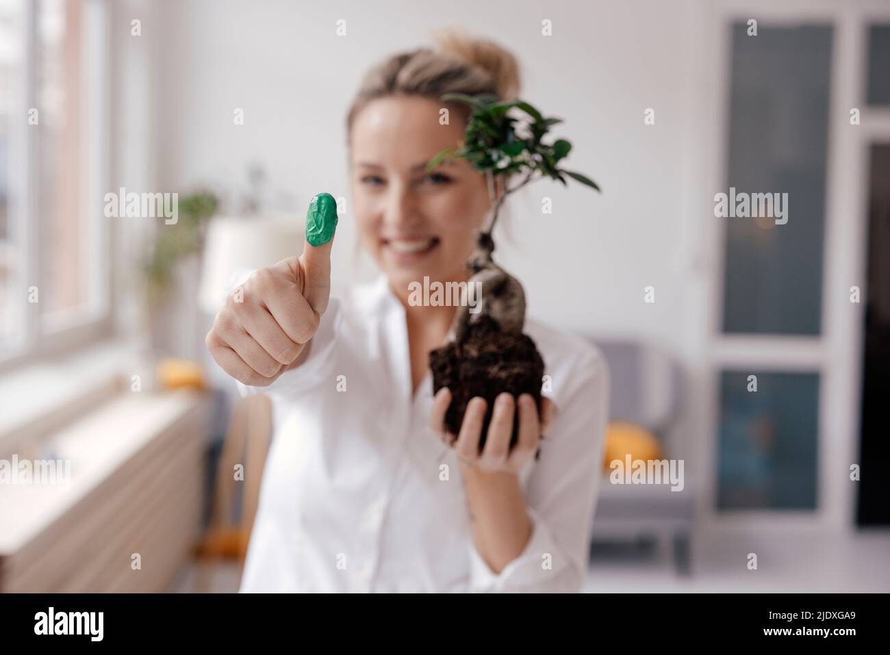 Happy businesswoman holding plant showing green thumb in office Stock Photo