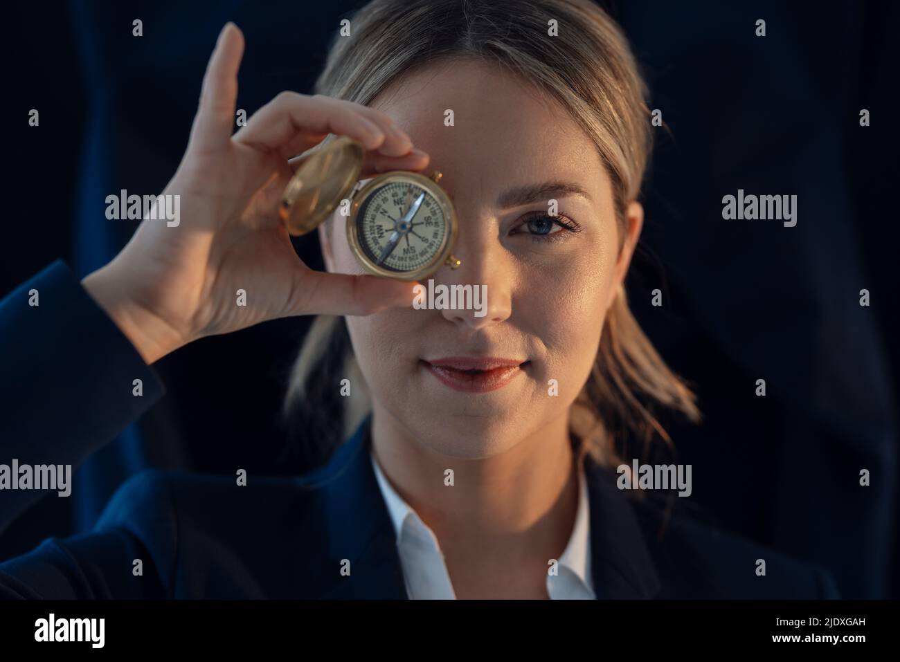 Businesswoman holding compass in front of eye against black background Stock Photo