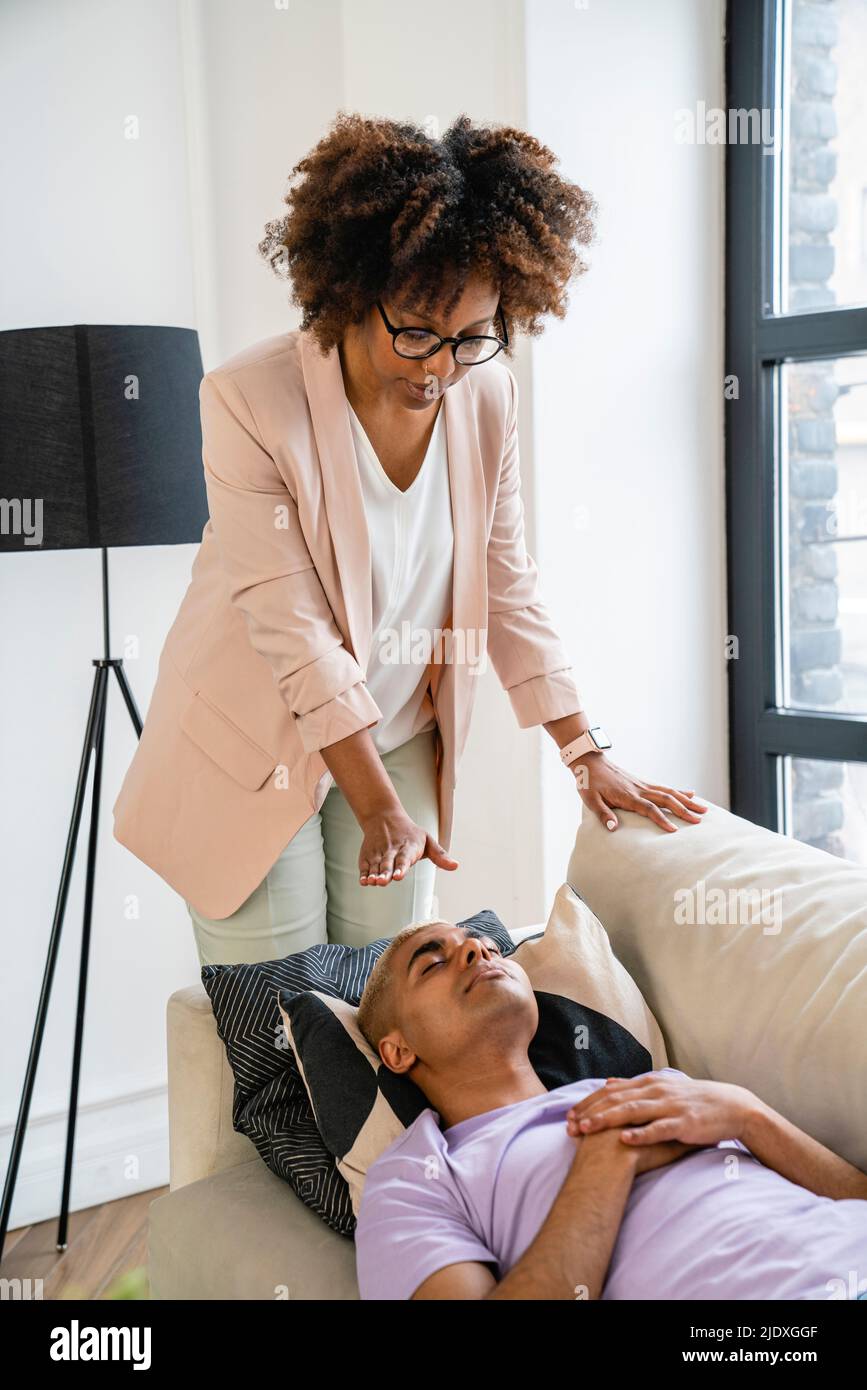 Young psychologist doing hypnosis therapy on patient lying on sofa Stock Photo