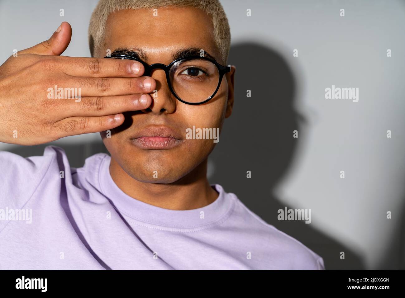 Young man covering eye with hand standing in front of wall Stock Photo