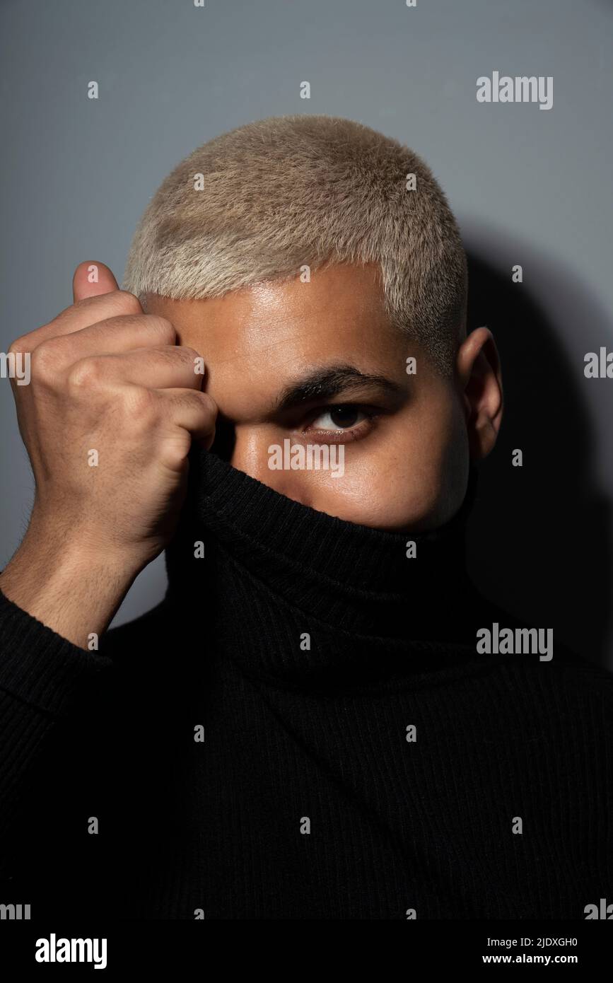 Young man covering face with turtleneck top against gray background Stock Photo