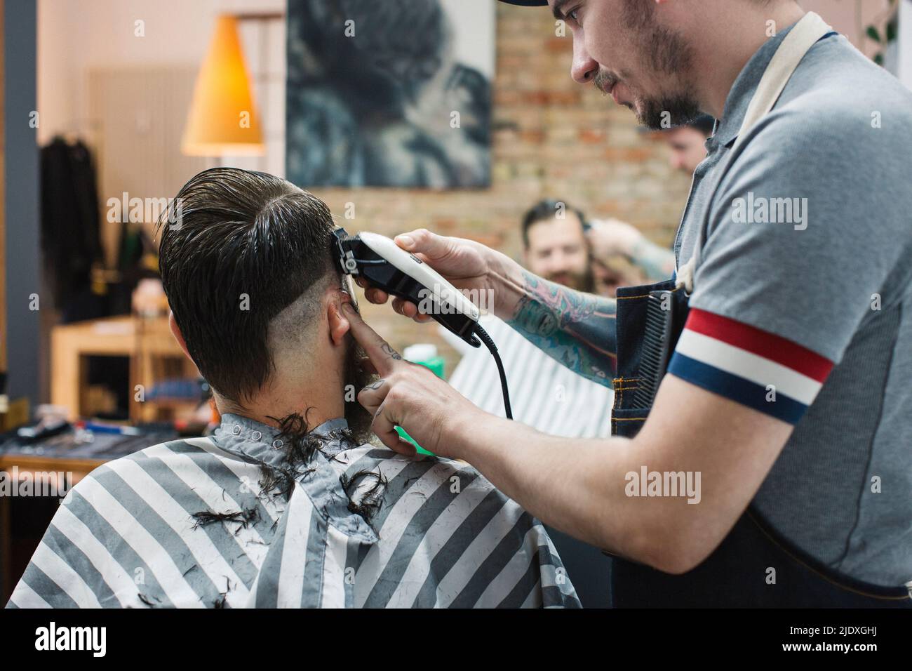 Hairdresser cutting hair of man with electric razor at barber shop ...