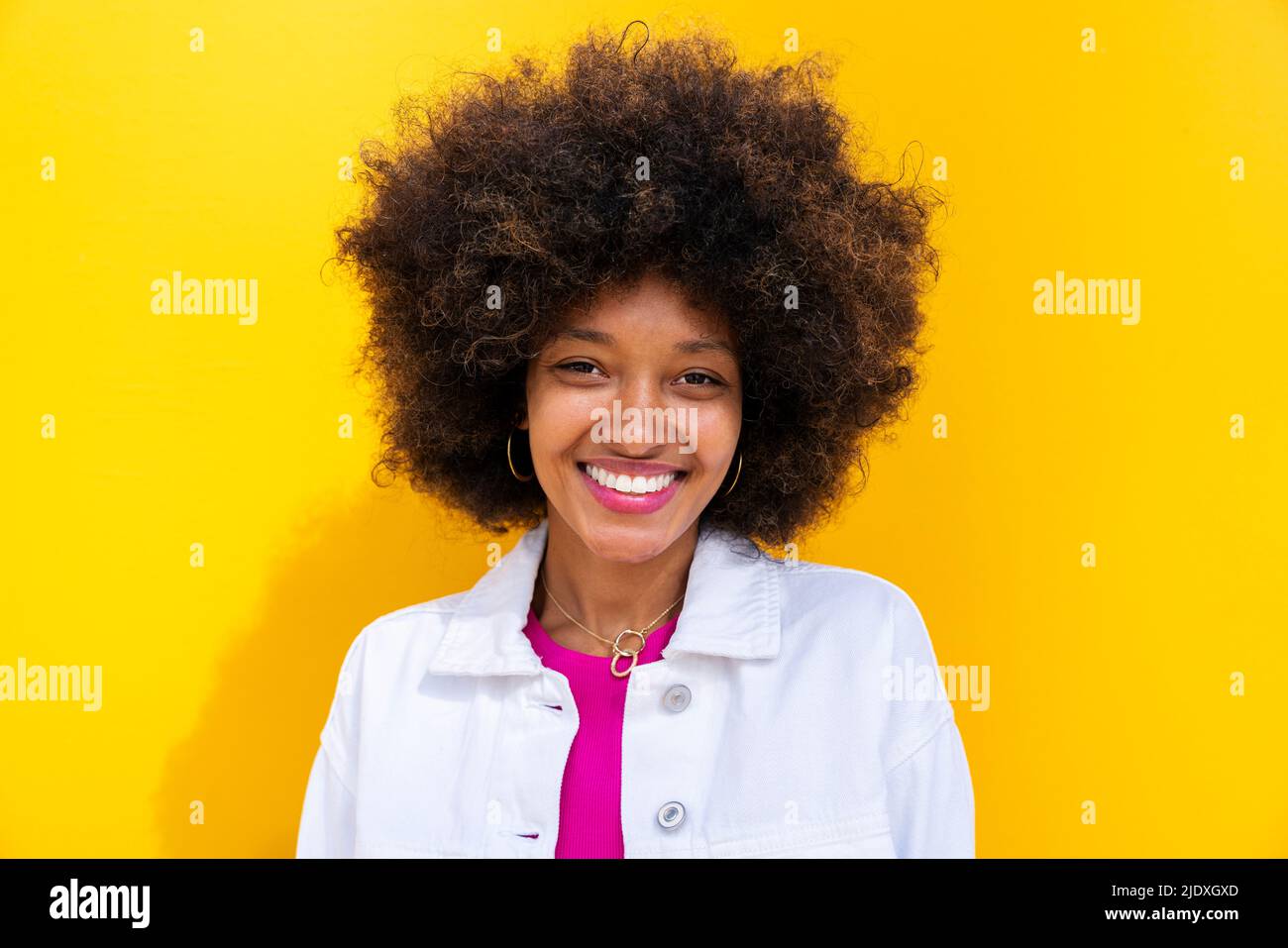 Smiling Afro woman in front of yellow wall Stock Photo - Alamy