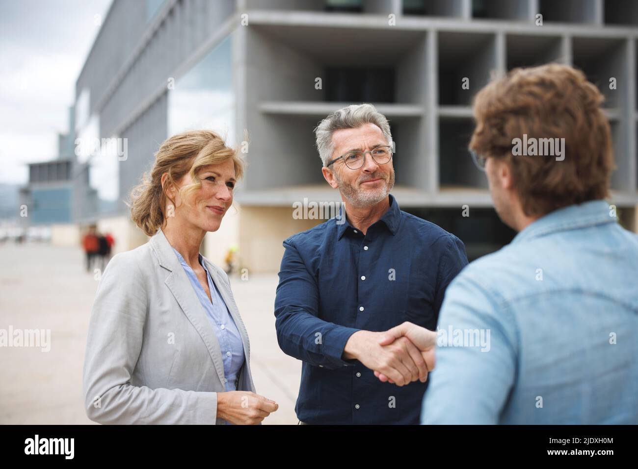 Smiling businessman shaking hand with colleague standing by businesswoman Stock Photo