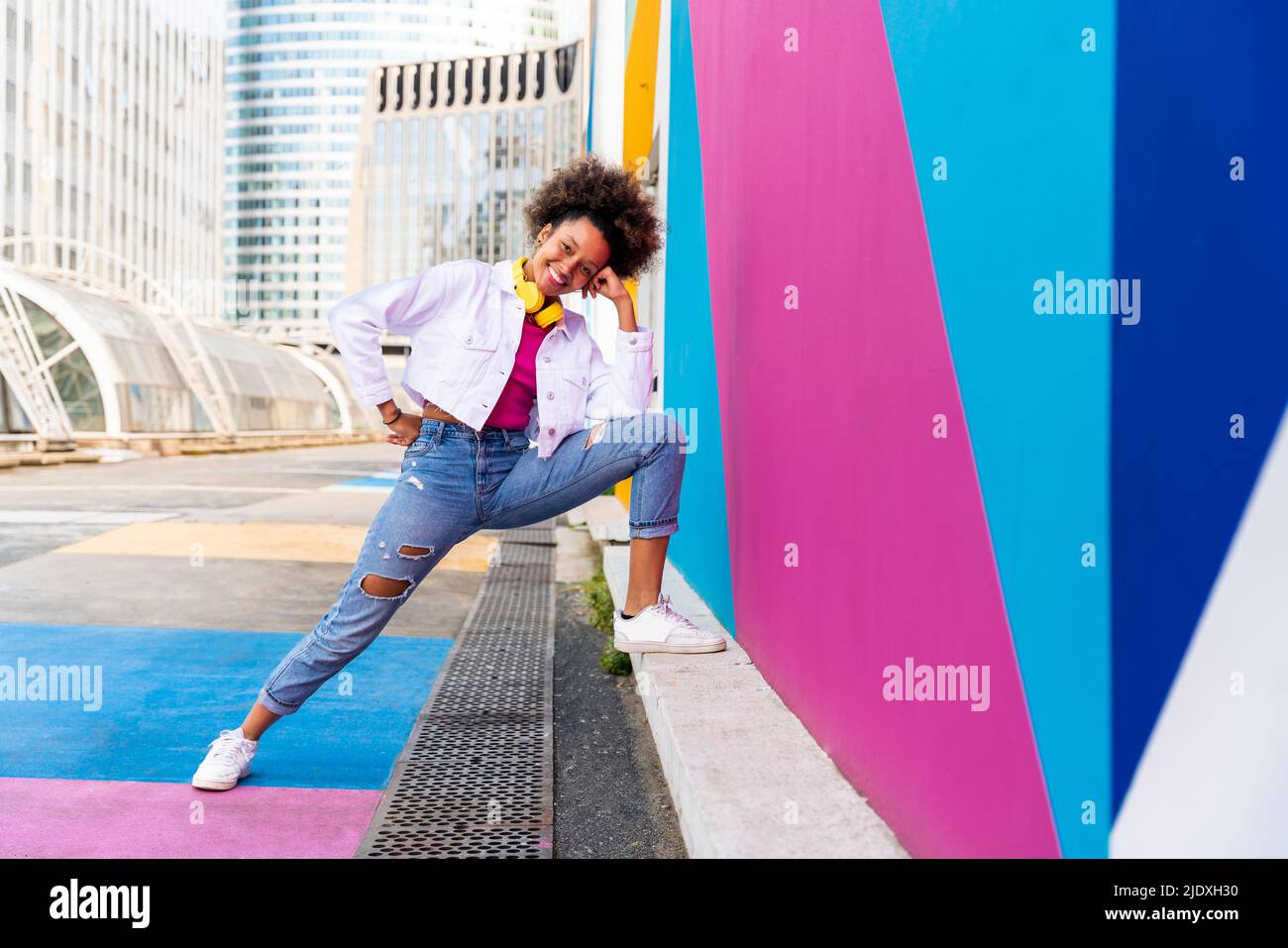 Smiling young Afro woman by colorful wall Stock Photo - Alamy