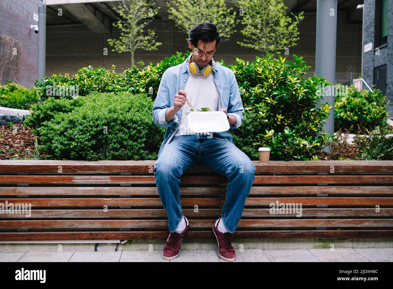 Man eating lunch sitting on bench in front of plants Stock Photo Alamy