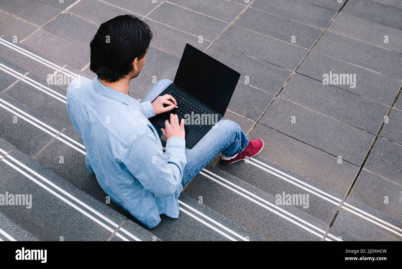 Man using laptop sitting on steps Stock Photo