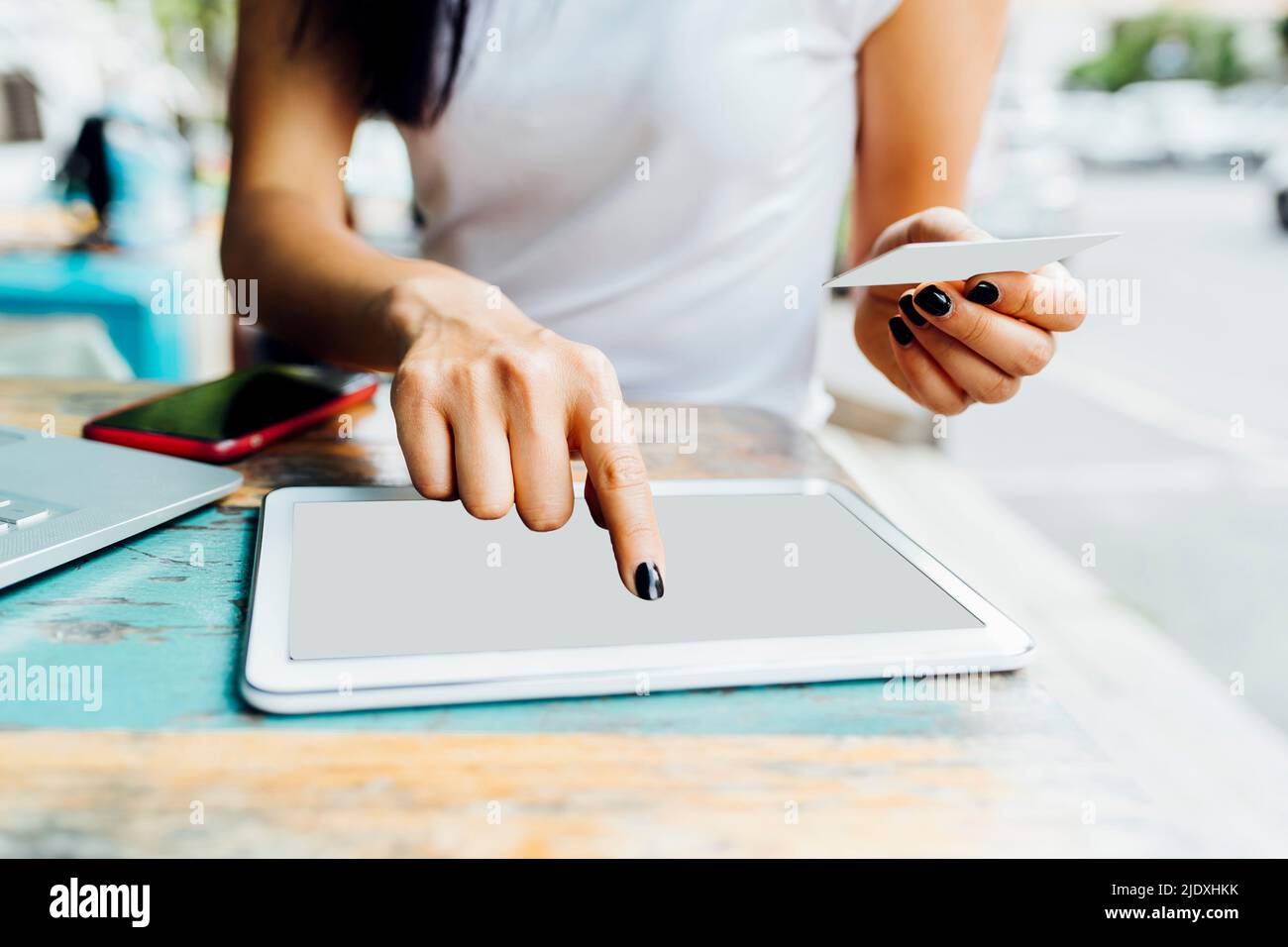 Hands of woman holding credit card making online payment through tablet PC at sidewalk cafe Stock Photo