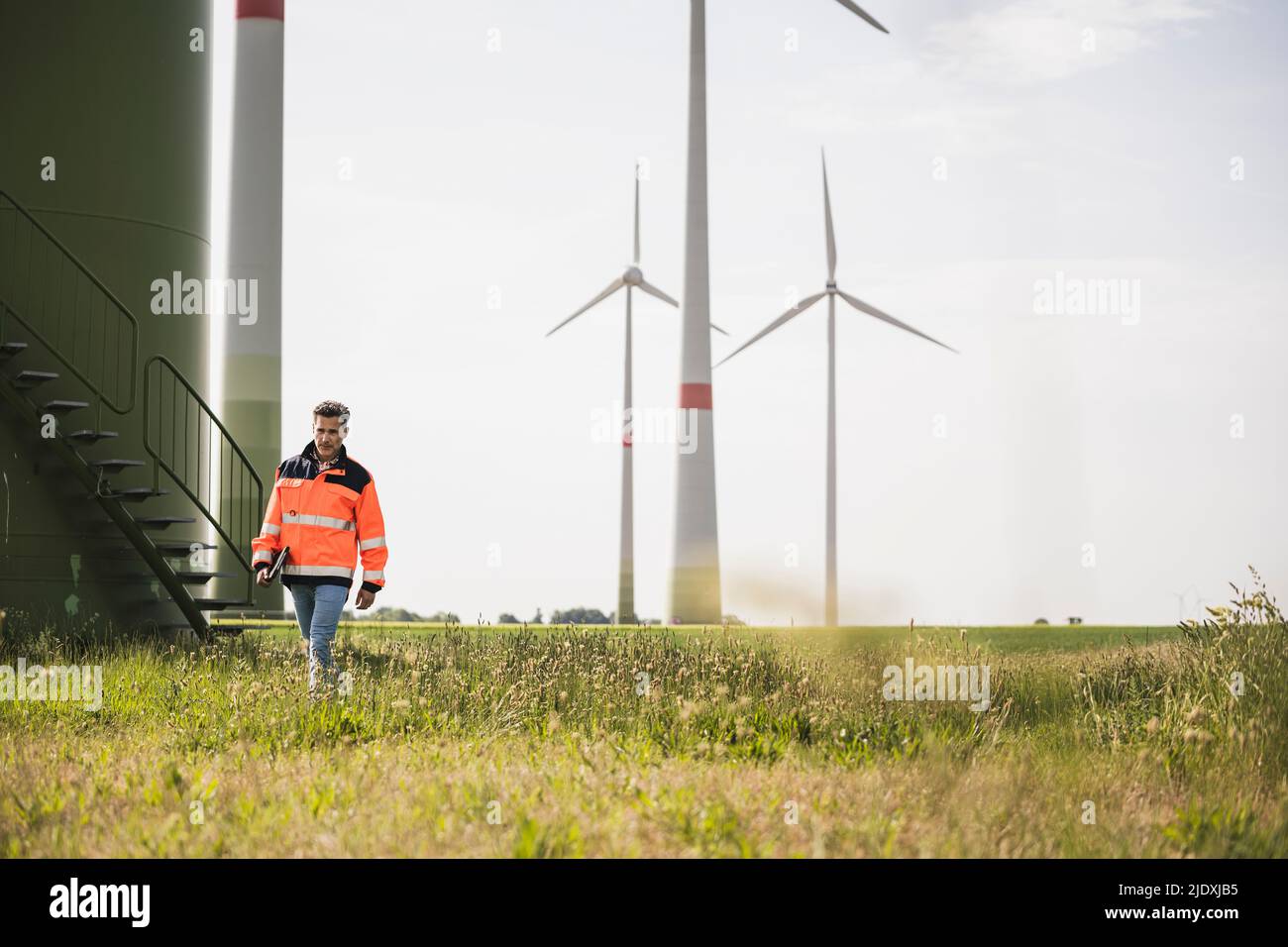 Engineer walking in front of wind turbines on field Stock Photo