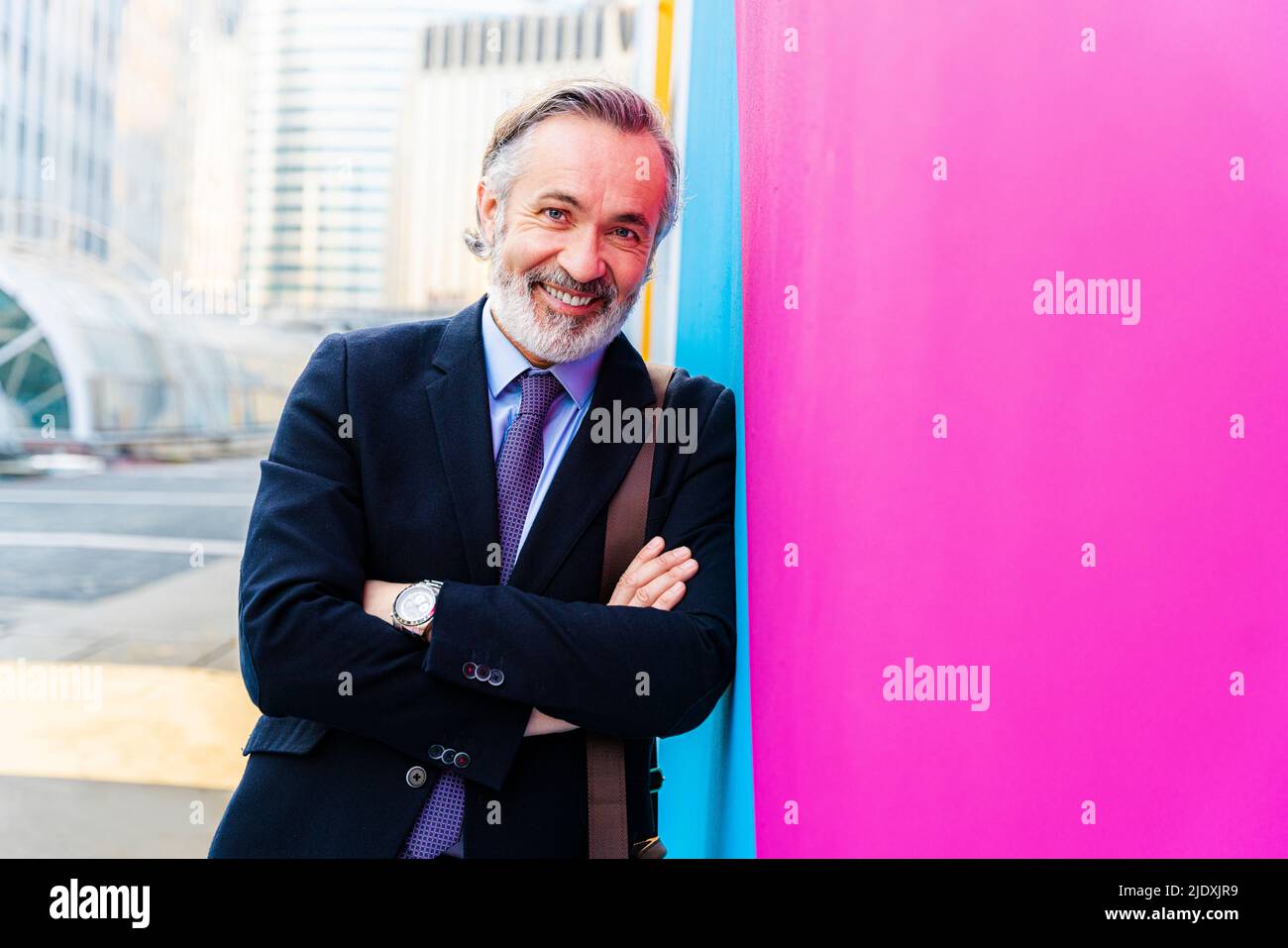 Happy businessman with arms crossed leaning on pink and blue wall Stock ...