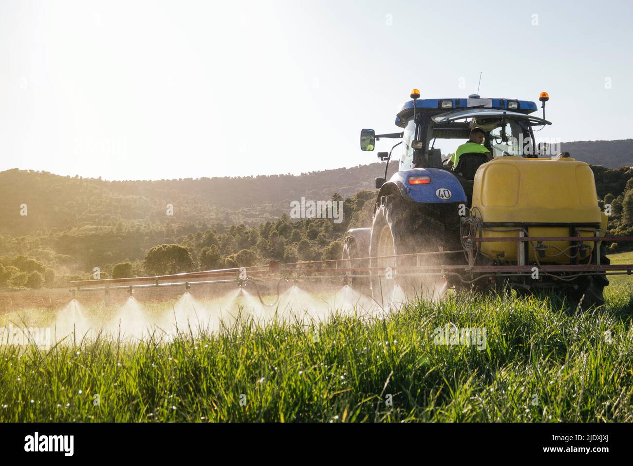 Young farmer spraying fertilizer through sprayer on tractor on field Stock Photo