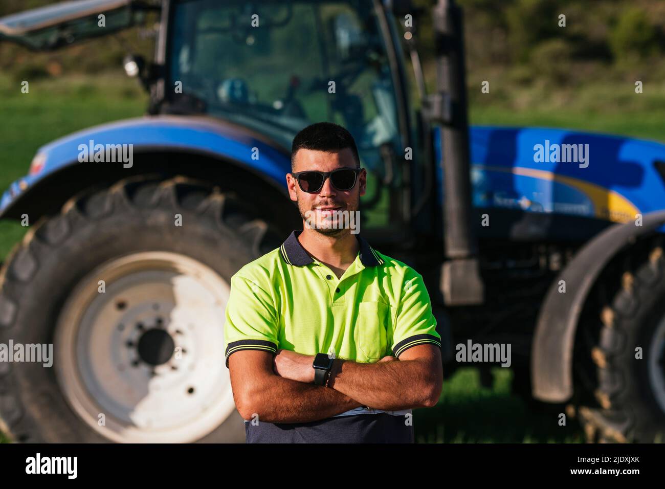 Young farmer standing with arms crossed in front of tractor Stock Photo ...