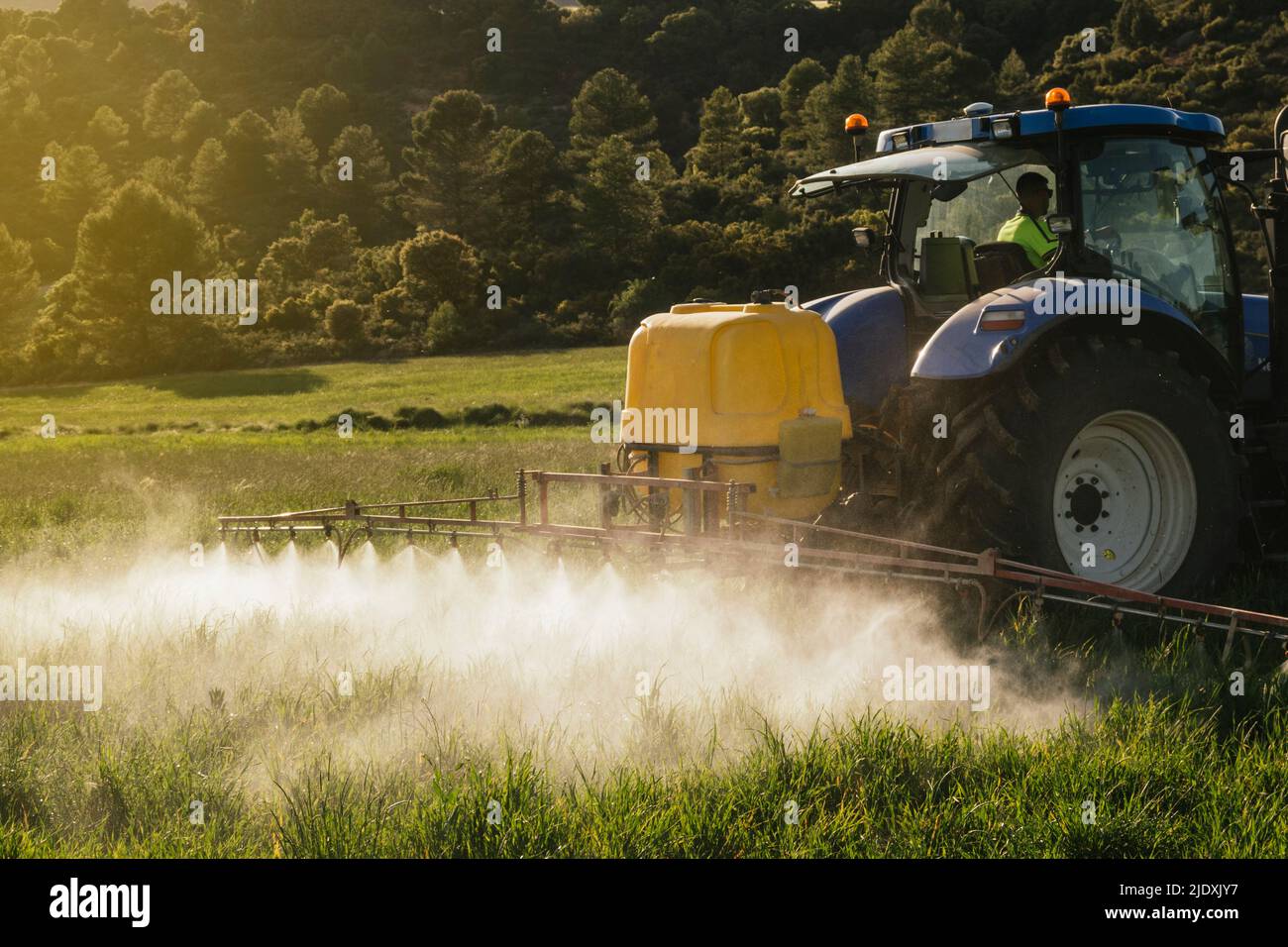 Farmer spraying fertilizer through sprayer on tractor on field Stock