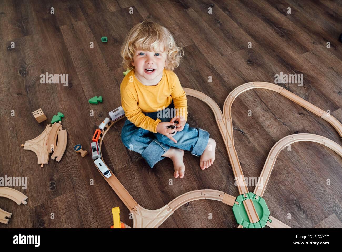 Happy boy with blond hair playing with toy train set at home Stock Photo