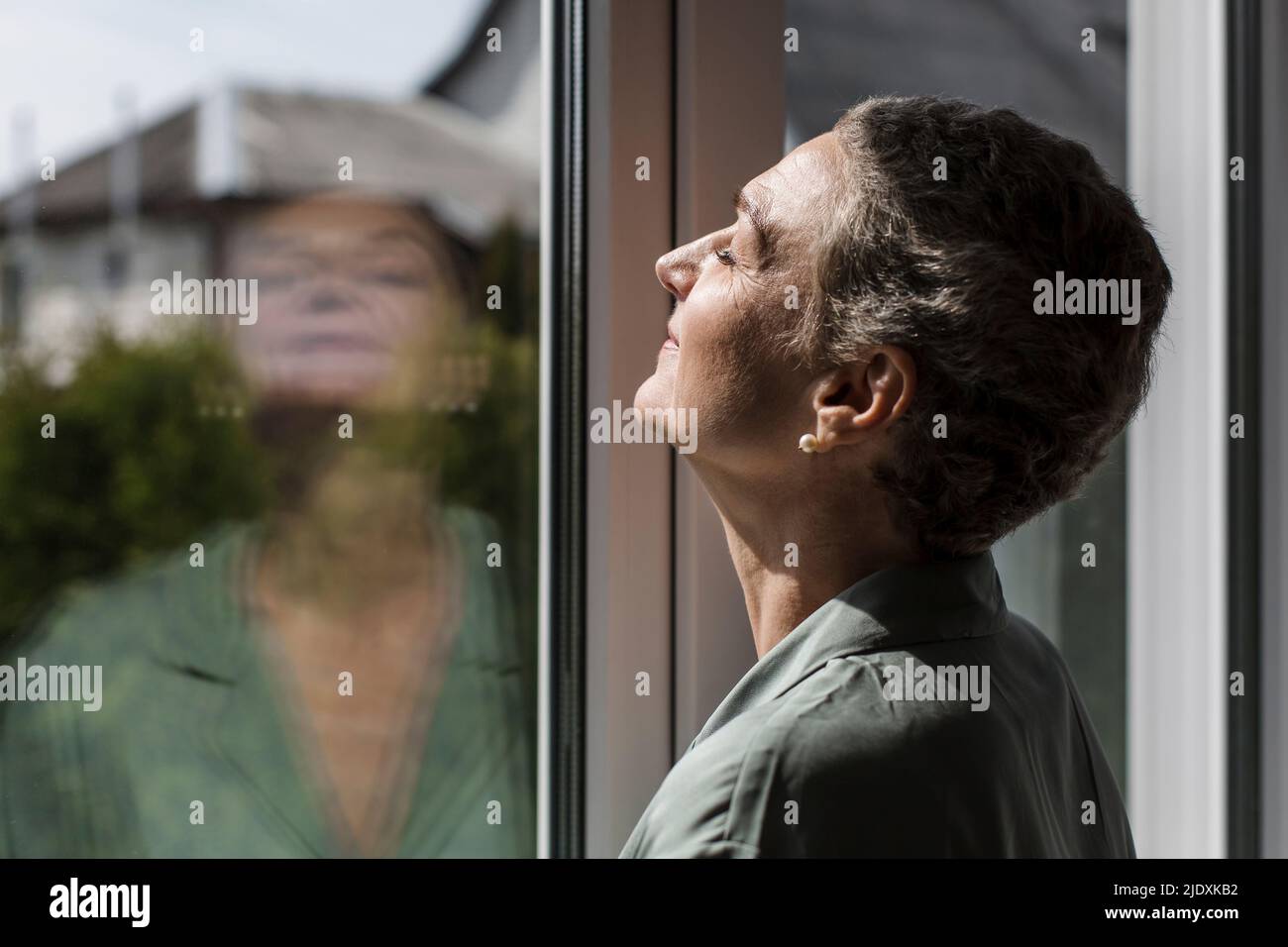 Mature woman with short grey hair at the window Stock Photo