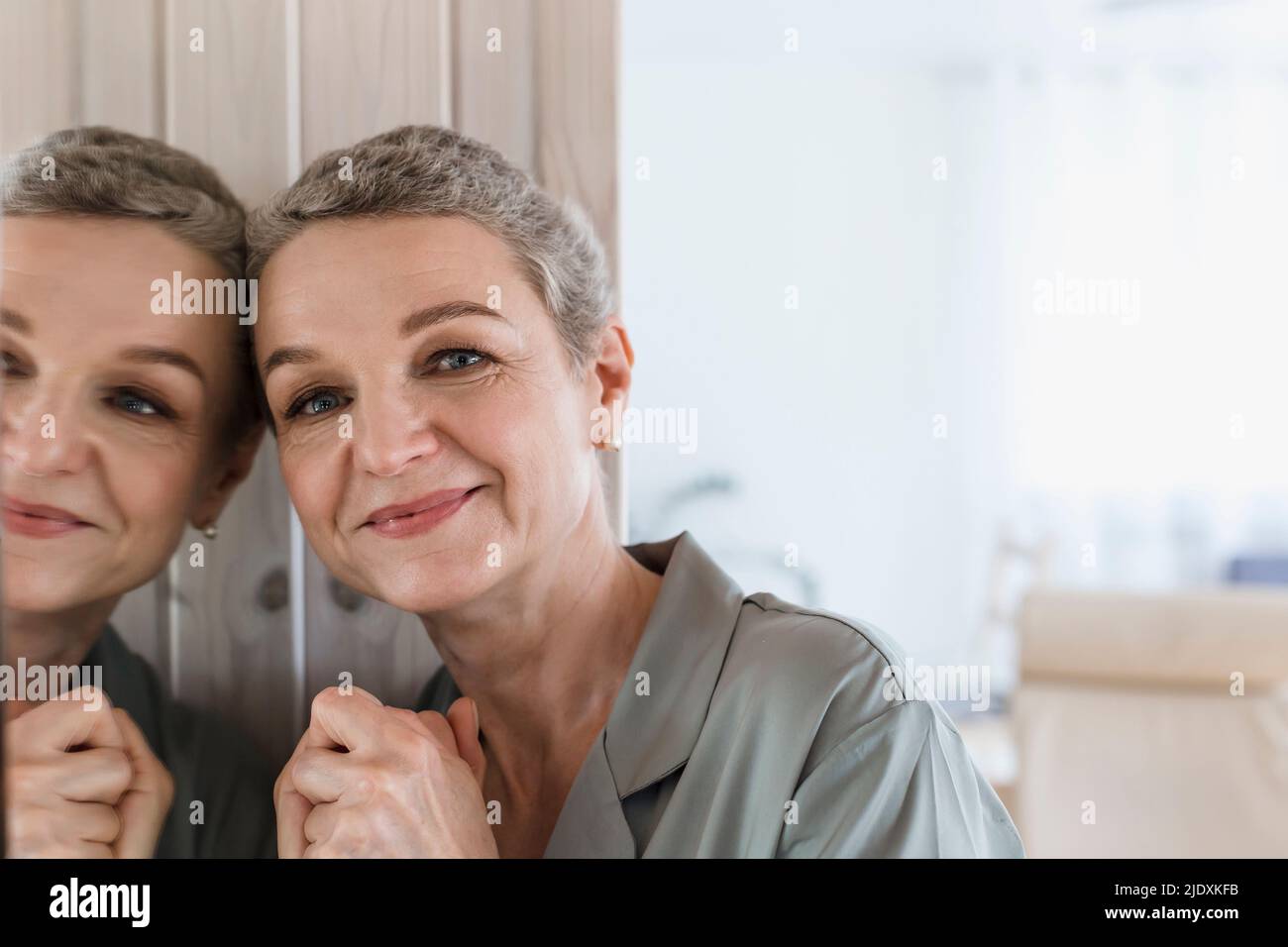 Portrait of mature woman with short grey hair leaning against mirror Stock Photo