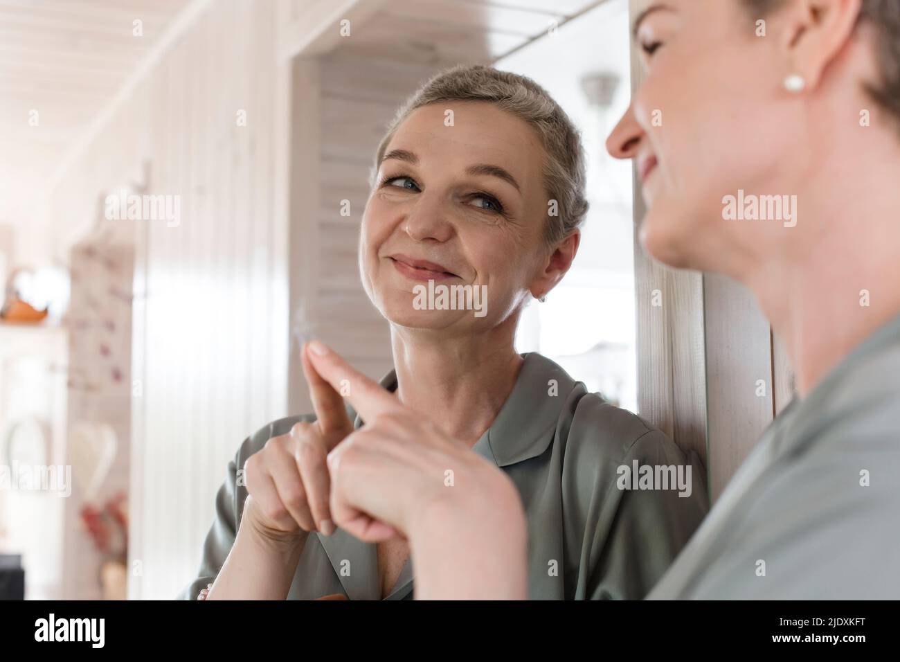 Confident mature woman looking in mirror at home Stock Photo