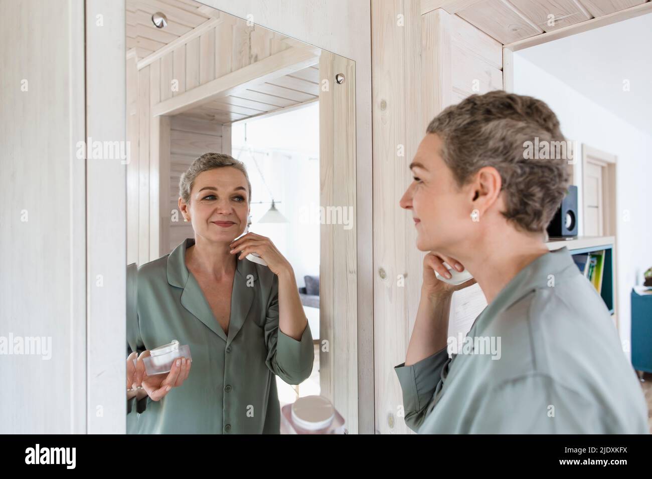 Mature woman looking in mirror applying face cream Stock Photo