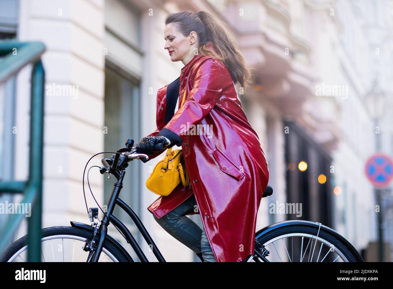 stylish middle aged woman in red rain coat outside in the city riding ...