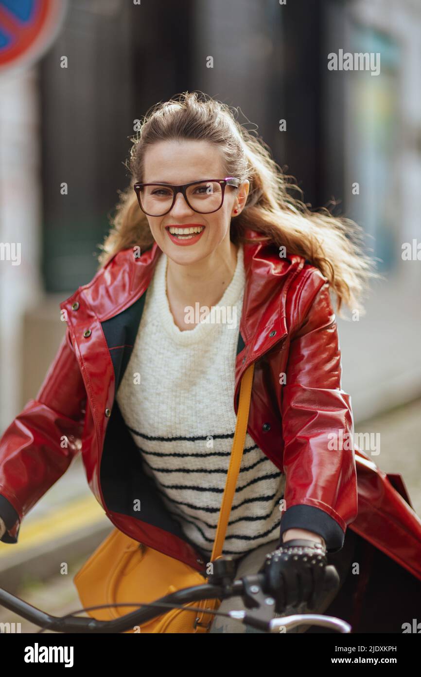 happy stylish 40 years old woman in red rain coat outside in the city ...