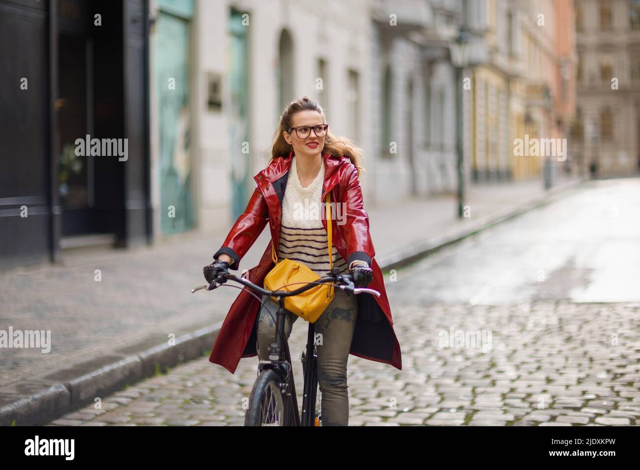 stylish woman in red rain coat outside on the city street riding ...