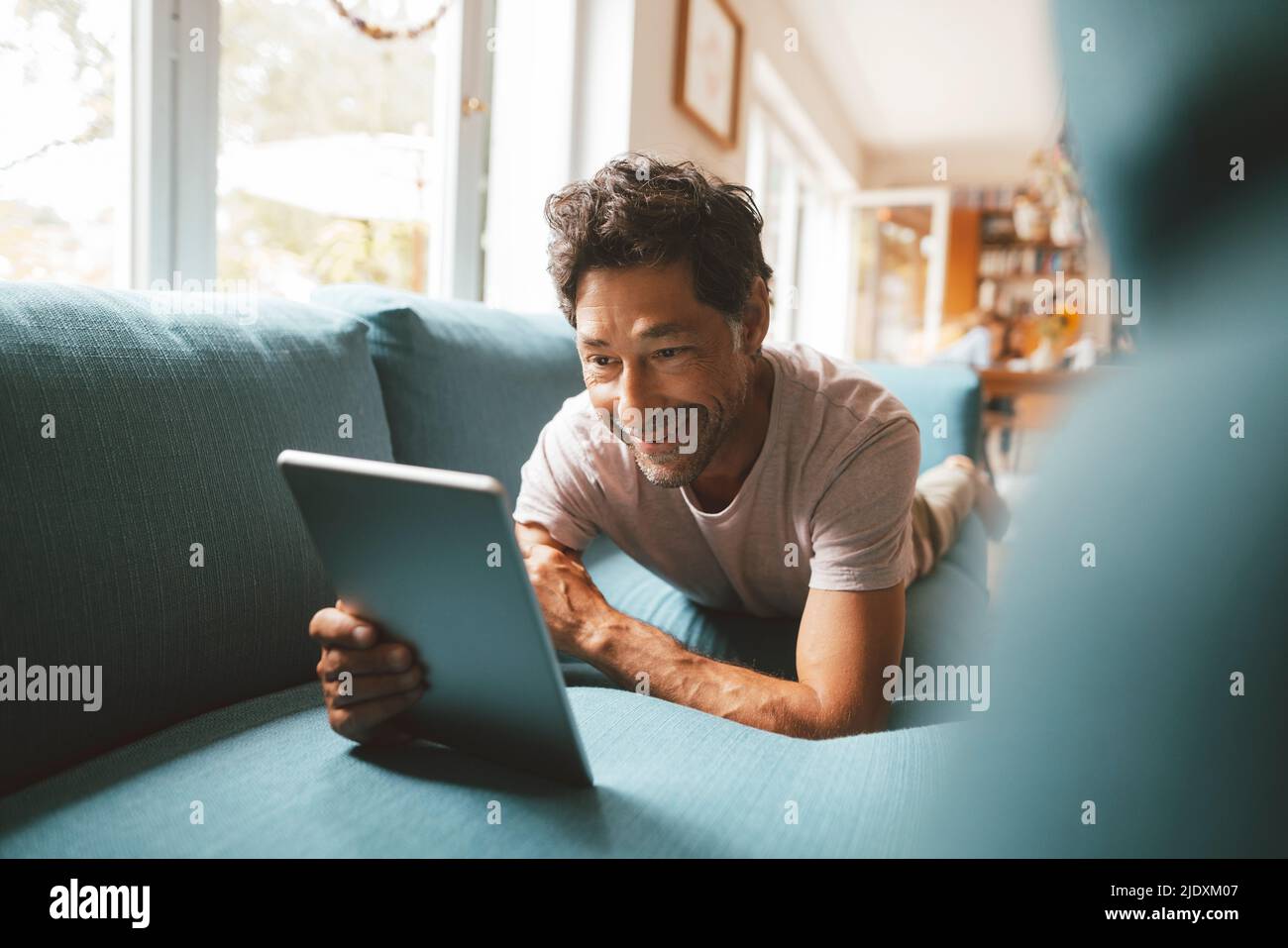 Happy man using tablet PC on sofa at home Stock Photo