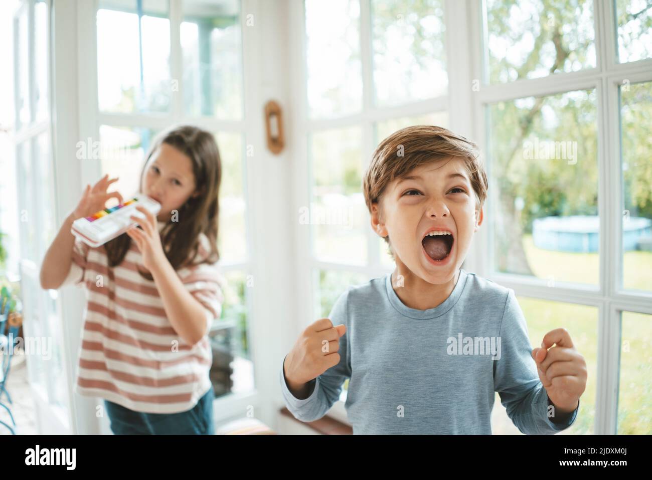 Boy screaming standing in front of sister playing musical instrument Stock Photo