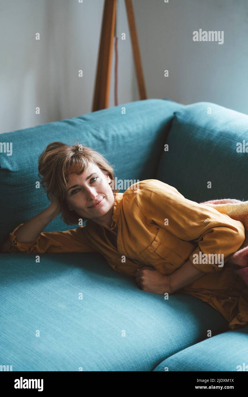 Smiling mature woman lying on sofa in living room at home Stock Photo ...