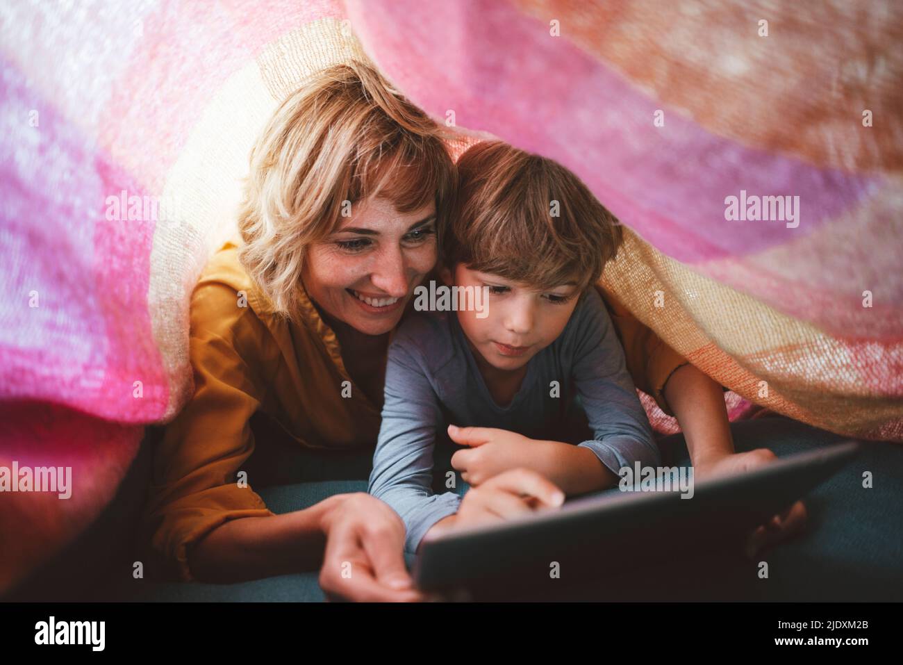 Cute boy with mother using tablet PC under blanket Stock Photo