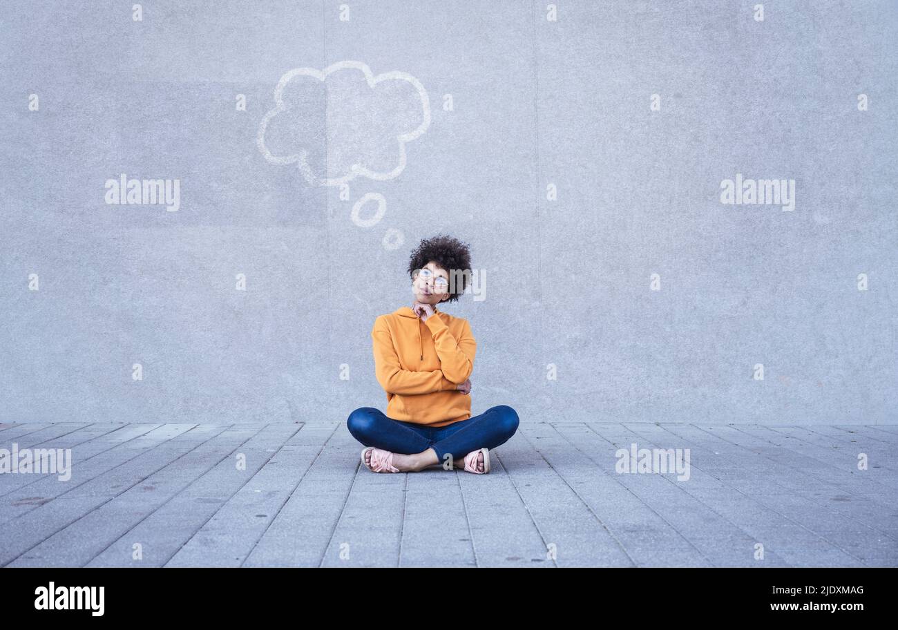 Woman sitting cross-legged on ground with empty thought bubble Stock Photo