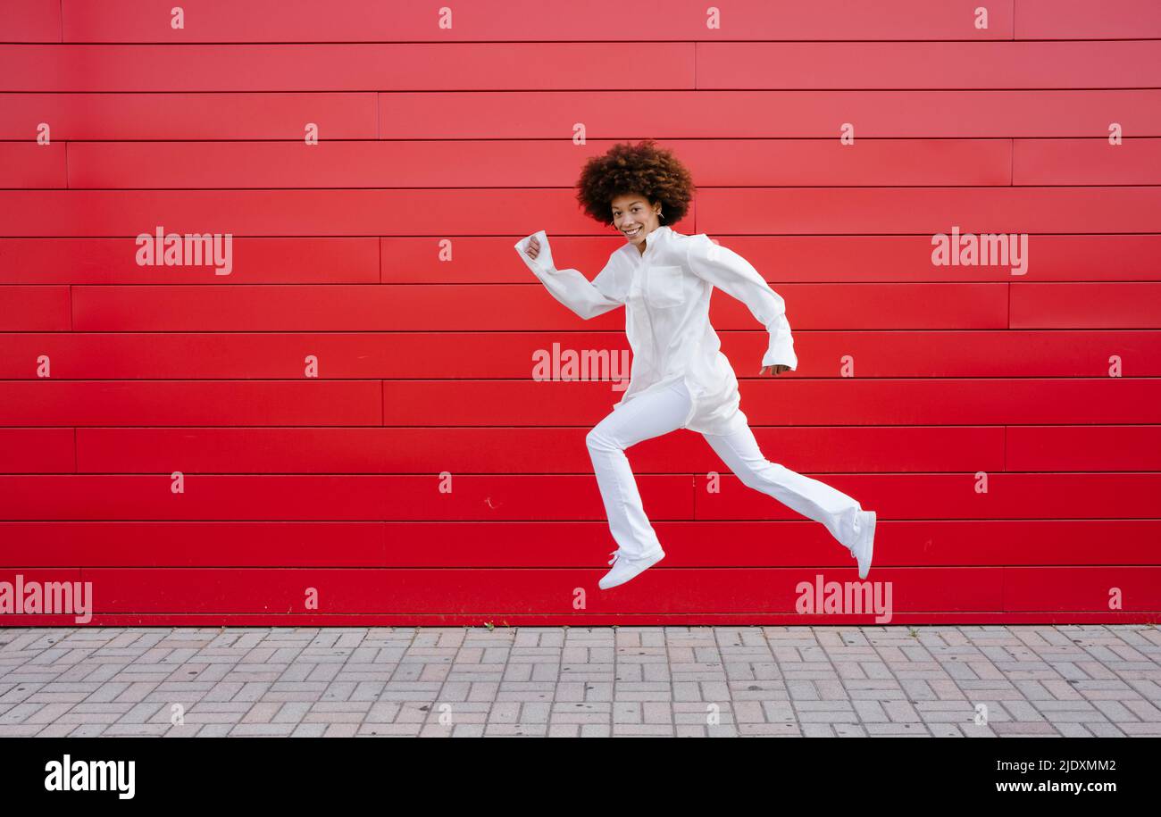 Afro woman jumping by red wall Stock Photo - Alamy