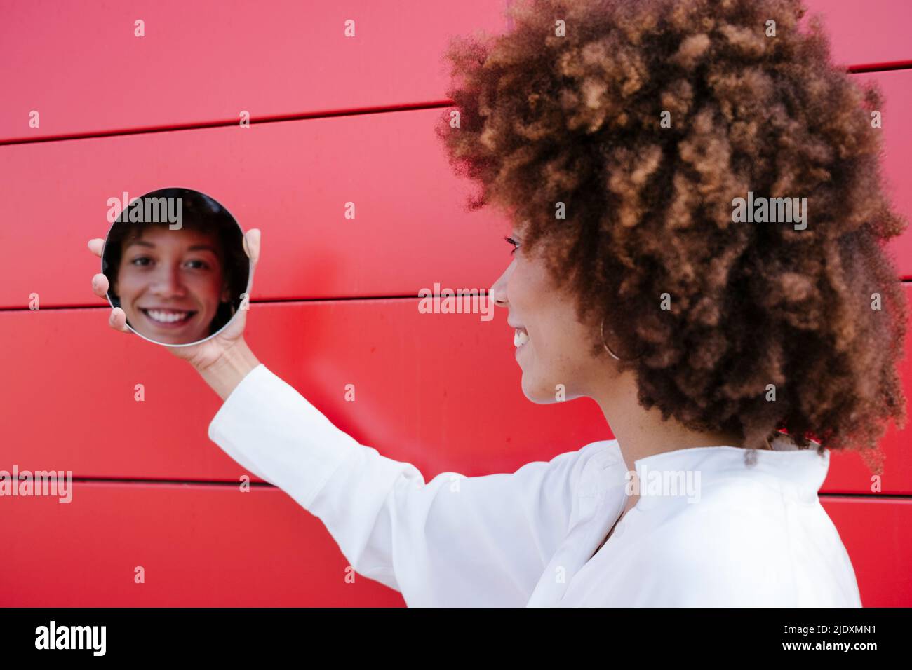 Reflection of woman's face on circular mirror by red wall Stock Photo