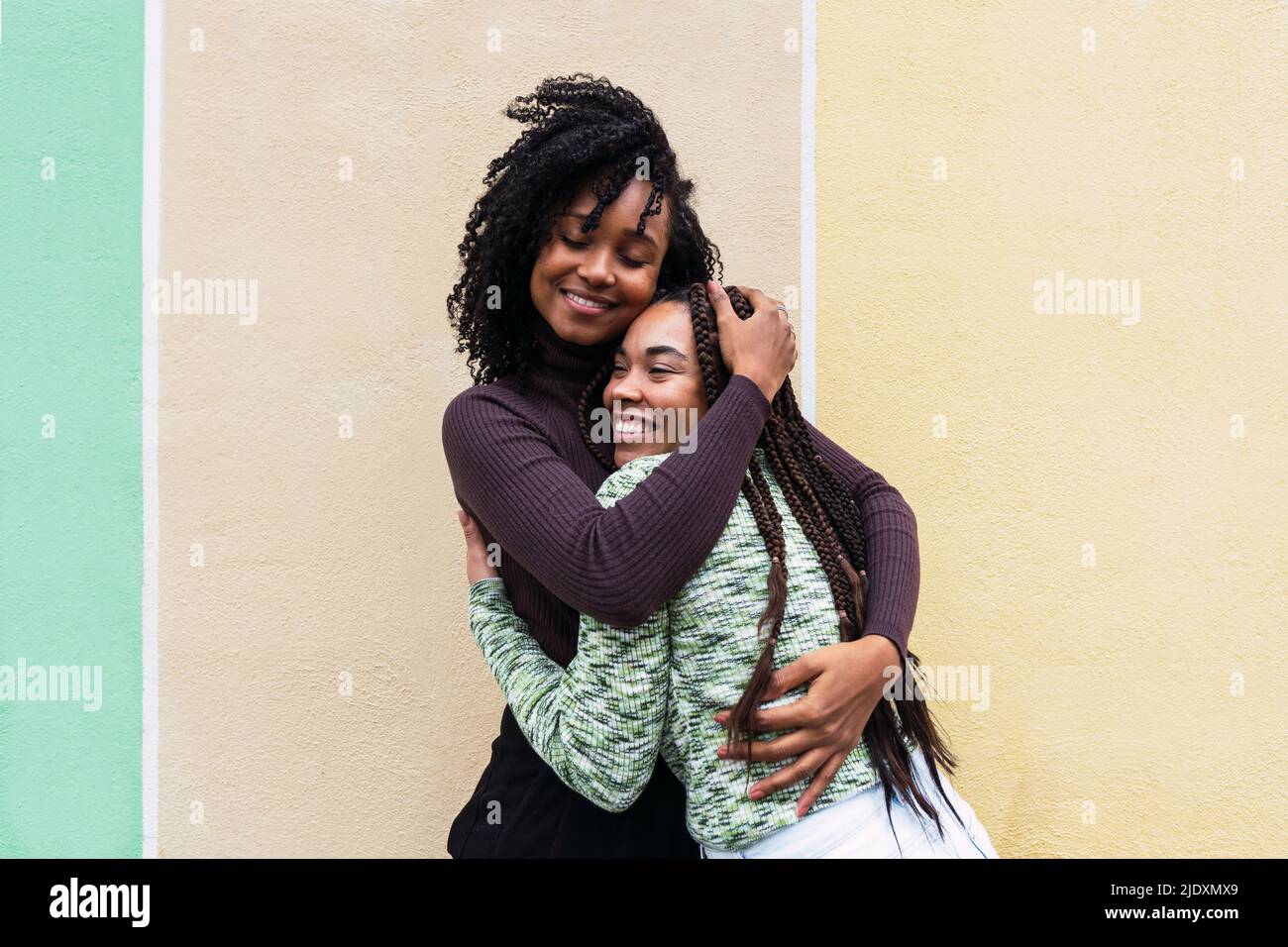 Happy female friends hugging each other standing in front of wall Stock ...