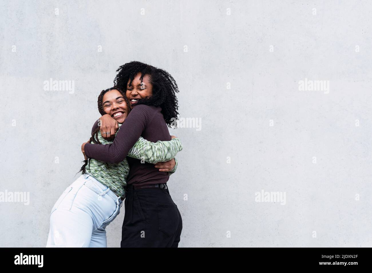 Cheerful female friends hugging each other in front of wall Stock Photo ...