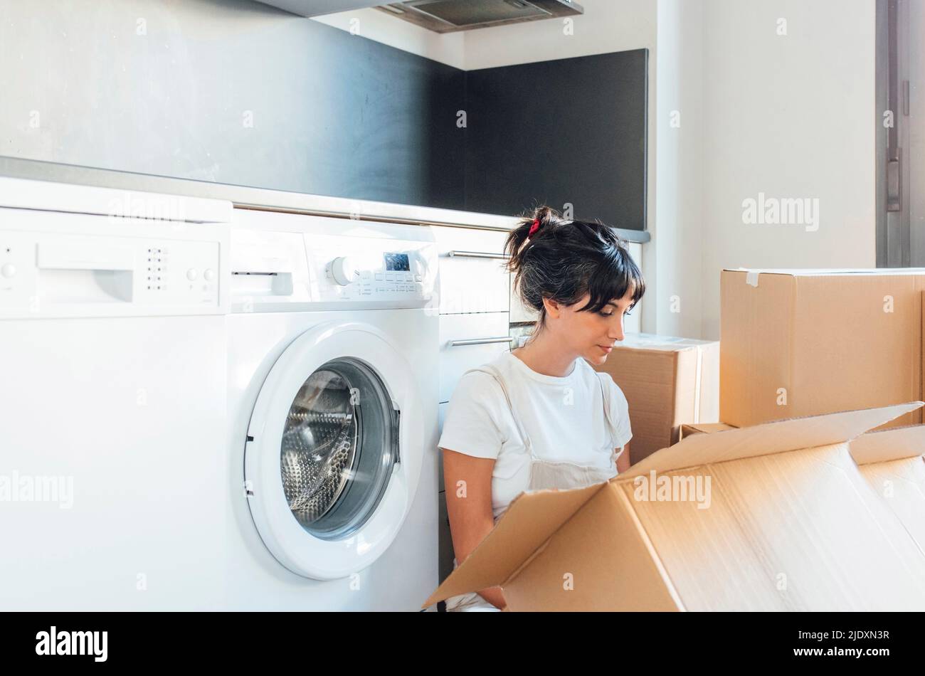 Woman looking in cardboard box sitting by washing machine in utility room  Stock Photo - Alamy