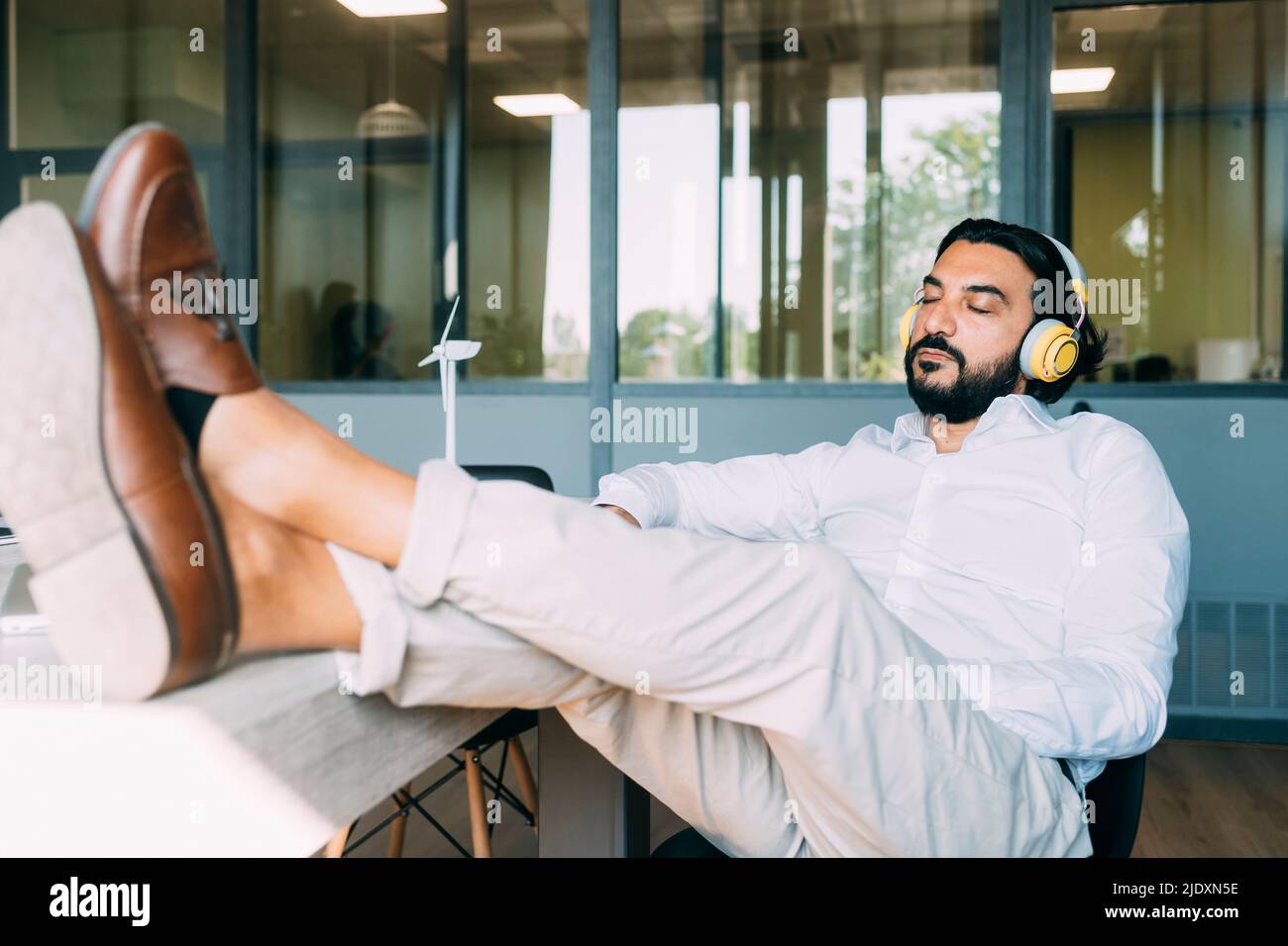 Mature businessman listening music on wireless headphones in office