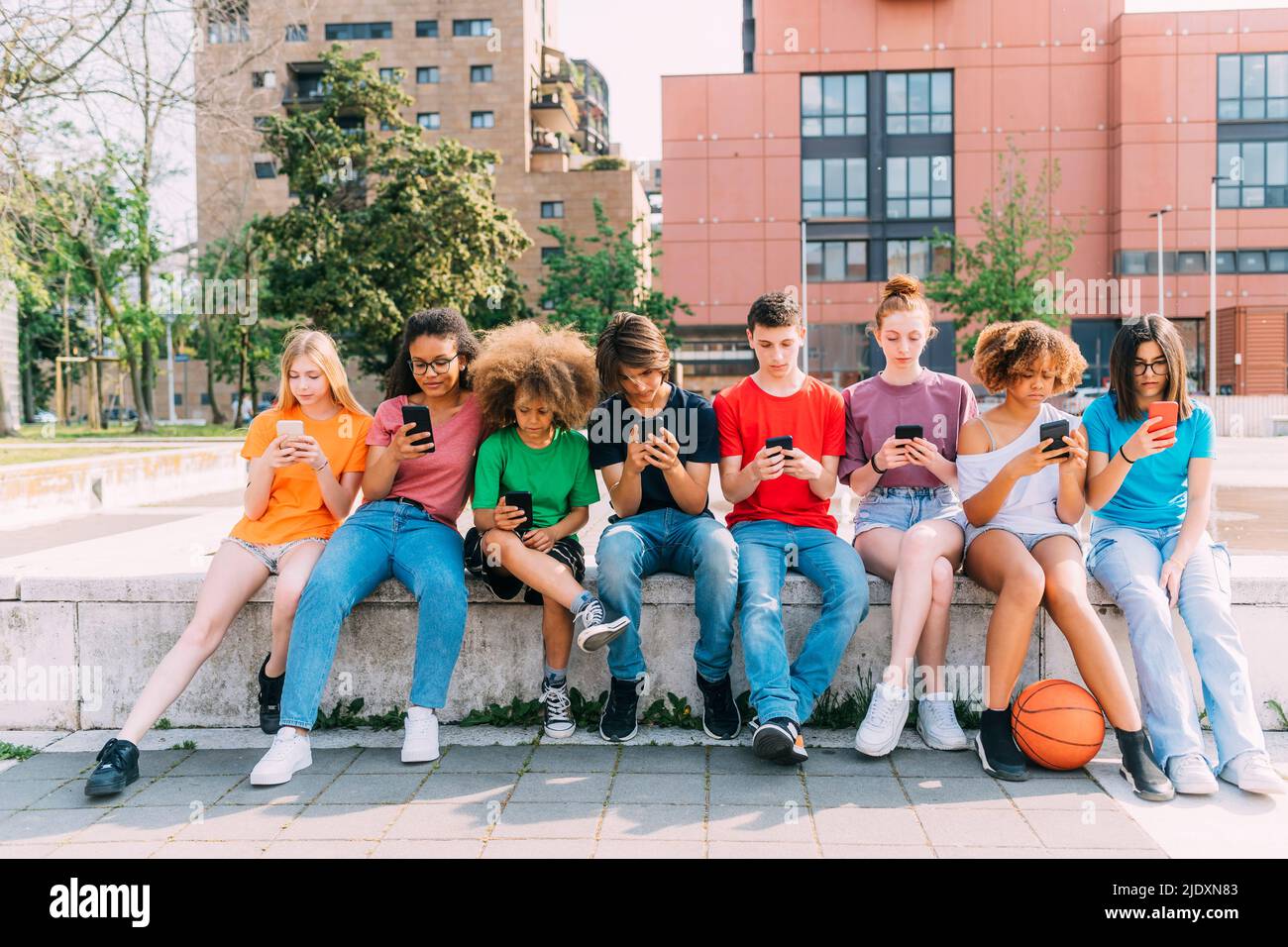 Friends using smart phones sitting on wall Stock Photo