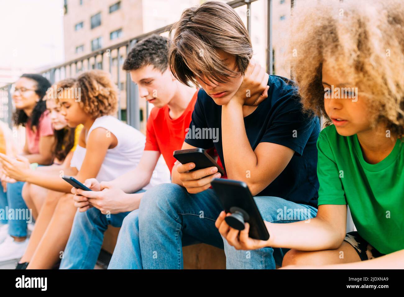 Friends using mobile phone sitting by railing Stock Photo