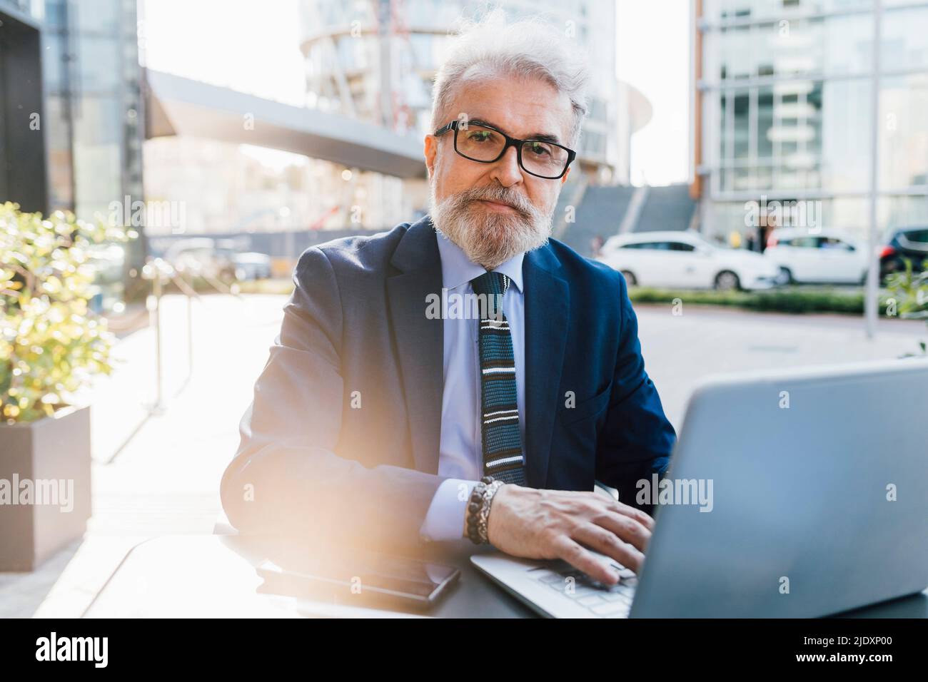 Senior businessman sitting with laptop outdoors Stock Photo